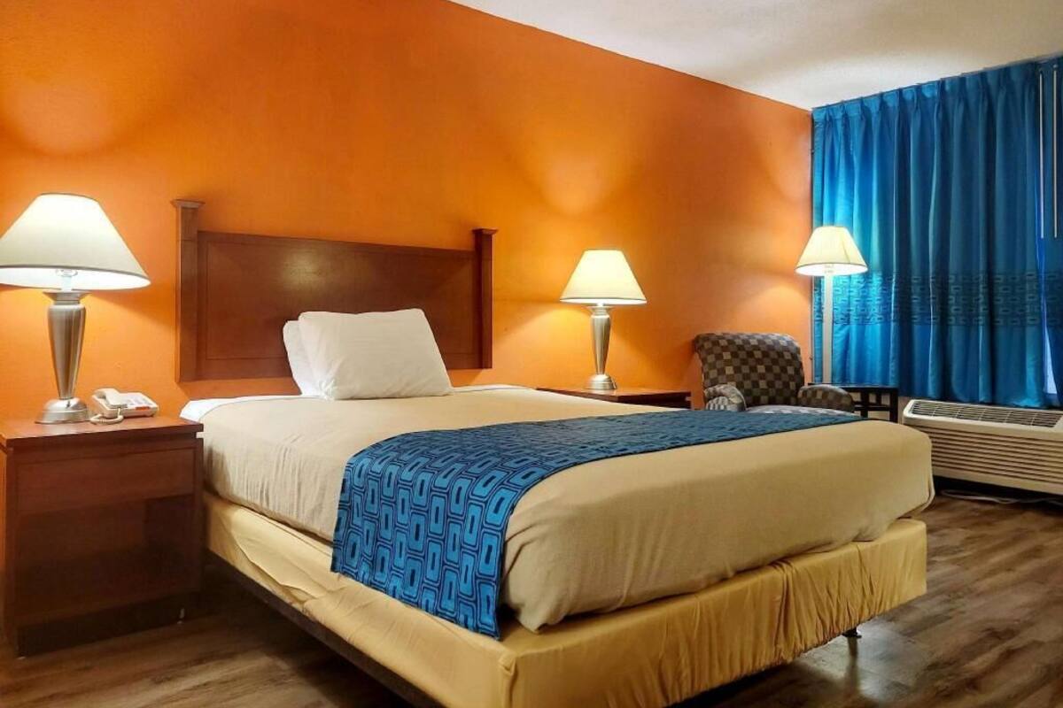 A hotel room with a large bed, two bedside lamps, a chair, and a window with curtains.