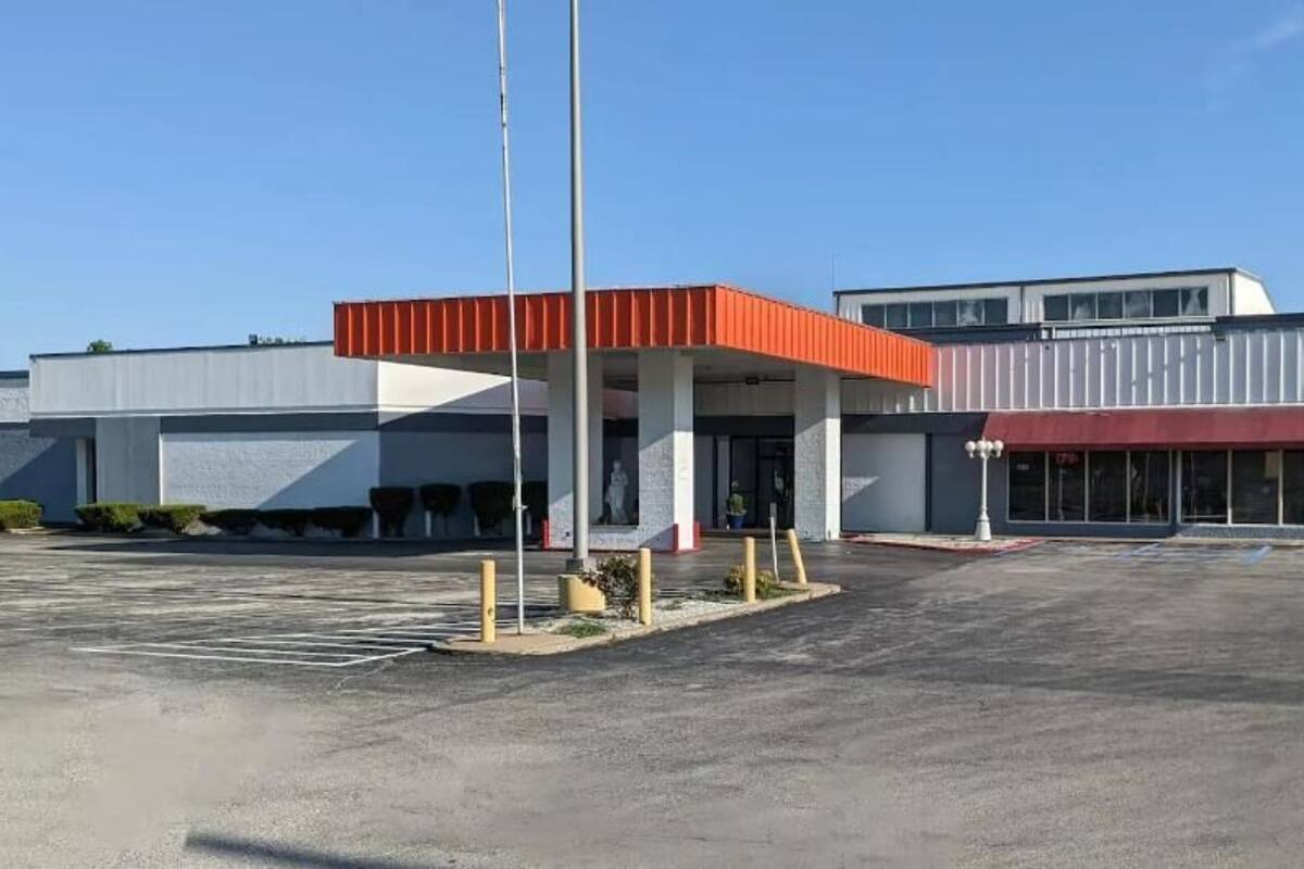 A gas station with a red canopy, a large parking lot, and a building with a flat roof and large windows.