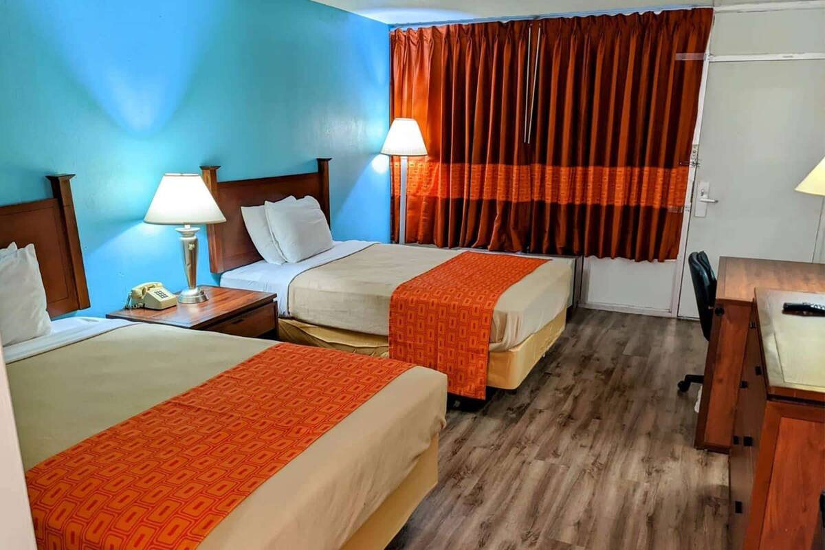 A hotel room with two beds, a desk, a chair, and a telephone.