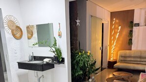 A modern living room with a black leather sofa, a black and white sink, and a potted plant. - Two minutes from the beach. House surrounded by nature. 500m² of private area. (São Sebastião)