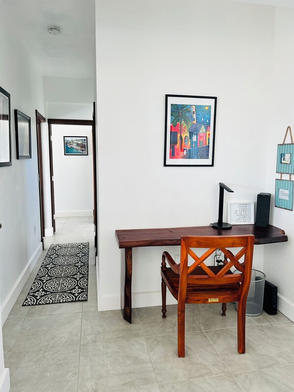 A hallway with a wooden dining table and chair, a black and white patterned rug, and a framed painting on the wall. - J&B’s Oceanview- Sleep 6 (Christiansted)