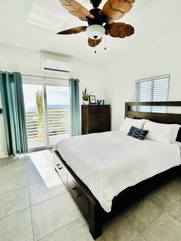 A bedroom with a large bed, a ceiling fan, a dresser, and a view through the window. - J&B’s Oceanview- Sleep 6 (Christiansted)