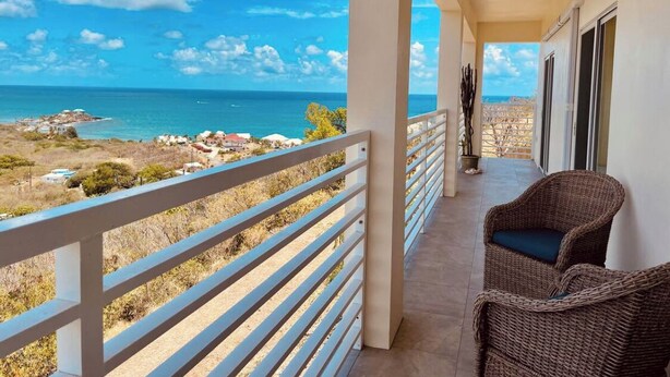 Uma varanda com vista para o oceano, mobiliário de vime e um corrimão.