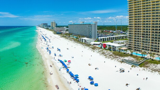A beach with a long stretch of white sand, clear turquoise water, and numerous blue umbrellas.