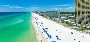 A beach with a long stretch of white sand, clear turquoise water, and numerous blue umbrellas.