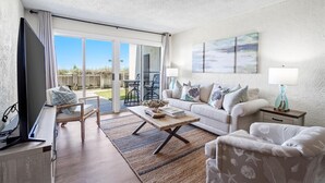 A living room with a sofa, coffee table, and TV. There is a sliding glass door leading to an outdoor area.