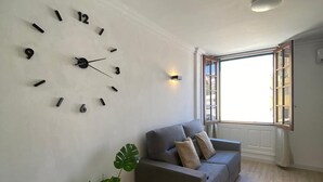 A living room with a wall clock, a gray sofa, a potted plant, and a window with a view. - Nice Apartment Playa Las Vistas. Free Wifi (Arona)