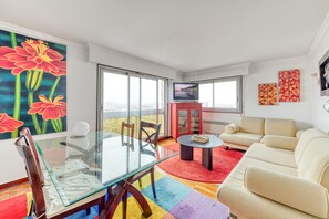 Una sala de estar moderna con una mesa de comedor de vidrio, un sofá color beige y alfombras de colores.