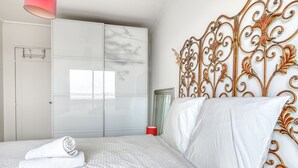 A neatly made bed with white linens, a red bedside lamp, and a decorative metal headboard. - Panoramic view of Paris (Paris)