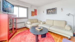 A living room with a beige sofa, a red cabinet, a black coffee table, and a TV on a stand. - Panoramic view of Paris (Paris)
