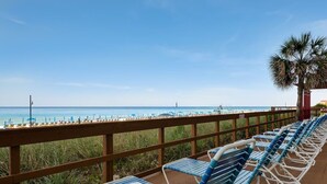Eine Strandterrasse mit Reihen von blauen und weißen Liegestühlen, einem hölzernen Geländer und Blick auf das Meer und Strandsonnenschirme.