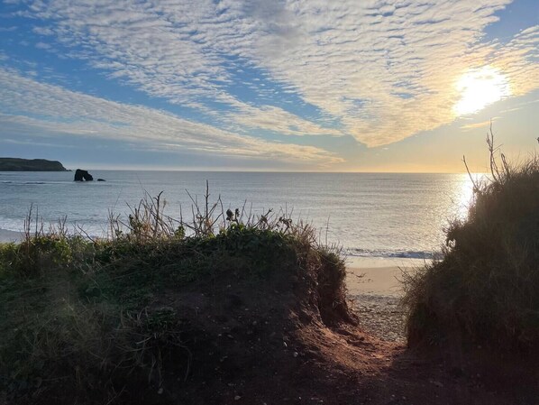 Un sendero costero que conduce al mar, bajo un cielo despejado y con una formación rocosa a lo lejos.