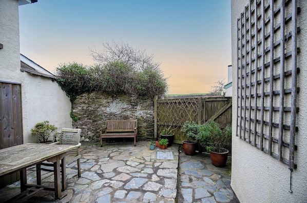 A stone patio with a wooden bench, a table, and potted plants.
