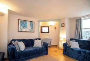 A cozy living room with two dark blue sofas, a small white table, and a framed picture on the wall.
