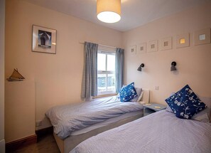 A bedroom with two beds, a window with curtains, wall-mounted lamps, and a framed picture.