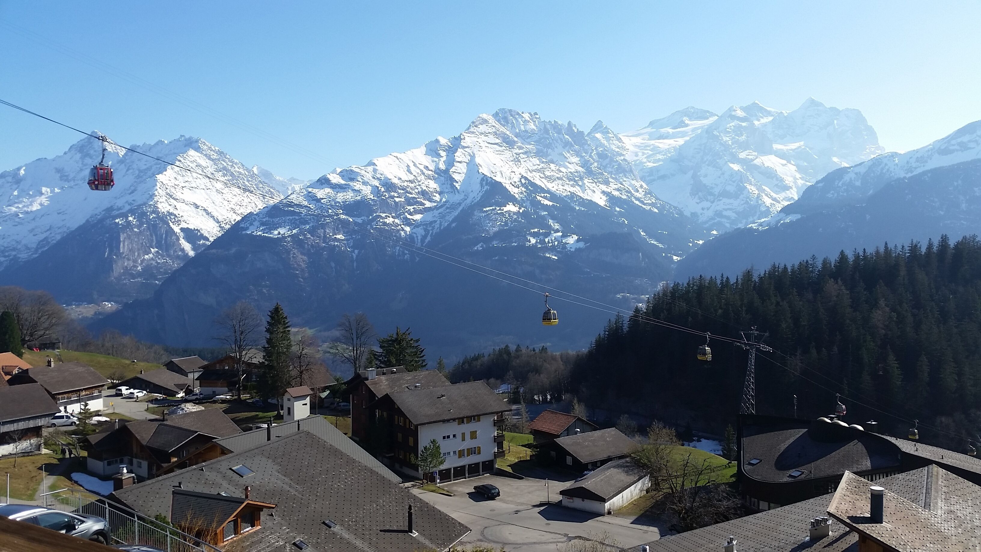 A mountain village with houses, a ski lift, and snow-covered peaks in the background.