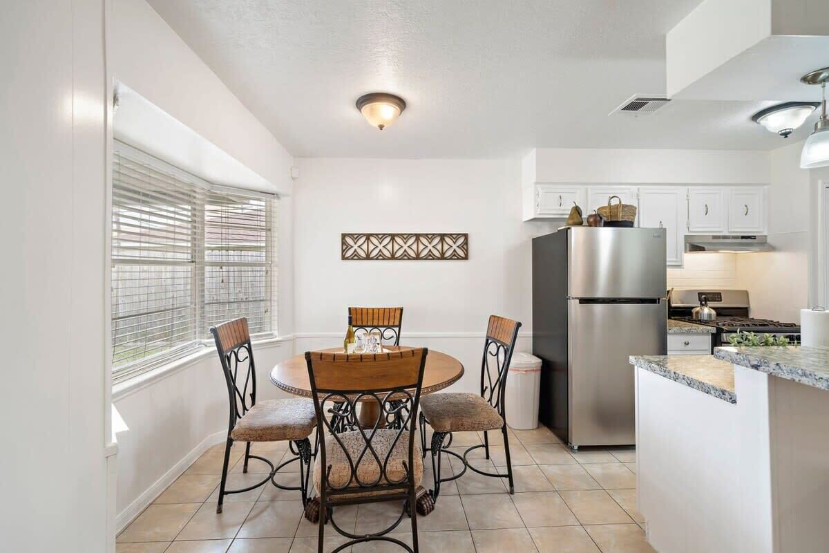 A modern kitchen with white cabinets, a stainless steel refrigerator, and a dining area with a round table and four chairs.