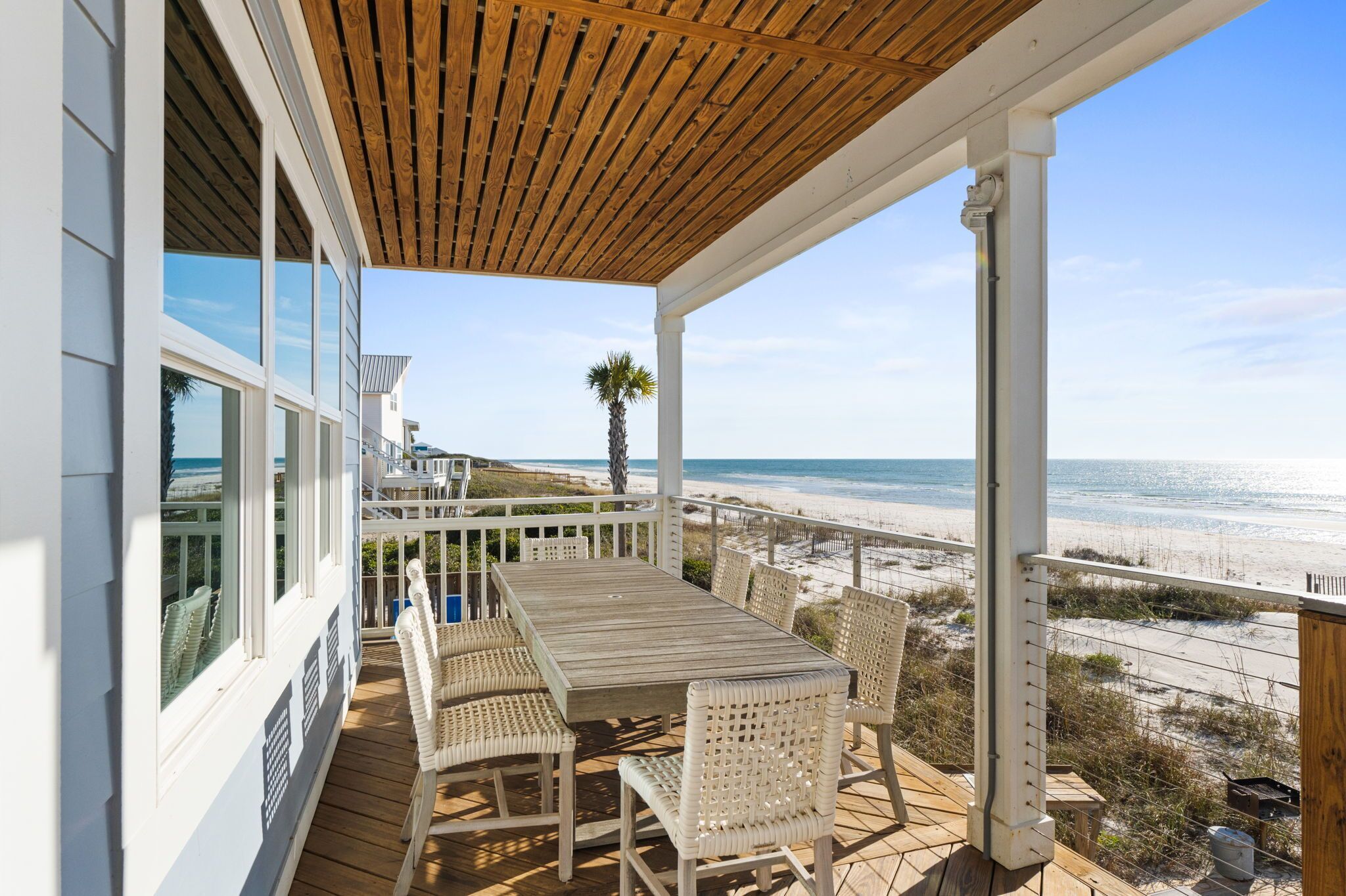 A wooden deck with a table and chairs overlooking a beach.