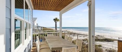 A wooden deck with a table and chairs overlooking a beach.