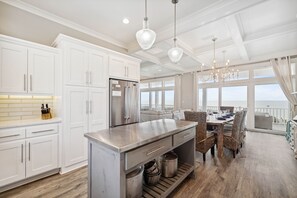 Eine moderne Küche mit weißen Schränken, einem Edelstahlkühlschrank und einem Essbereich mit Korbstühlen und einem Holztisch.