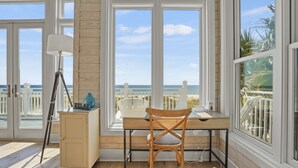A room with a desk, chair, lamp, and large windows overlooking a beach. - Island Life: Beachfront home, Sleeps 28, Pool, Pet-friendly, All the amenities! (St. George Island)