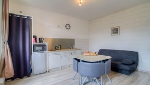 Un espacio habitable compacto con kitchenette, una mesa de comedor con sillas, un sofá y una cortina.