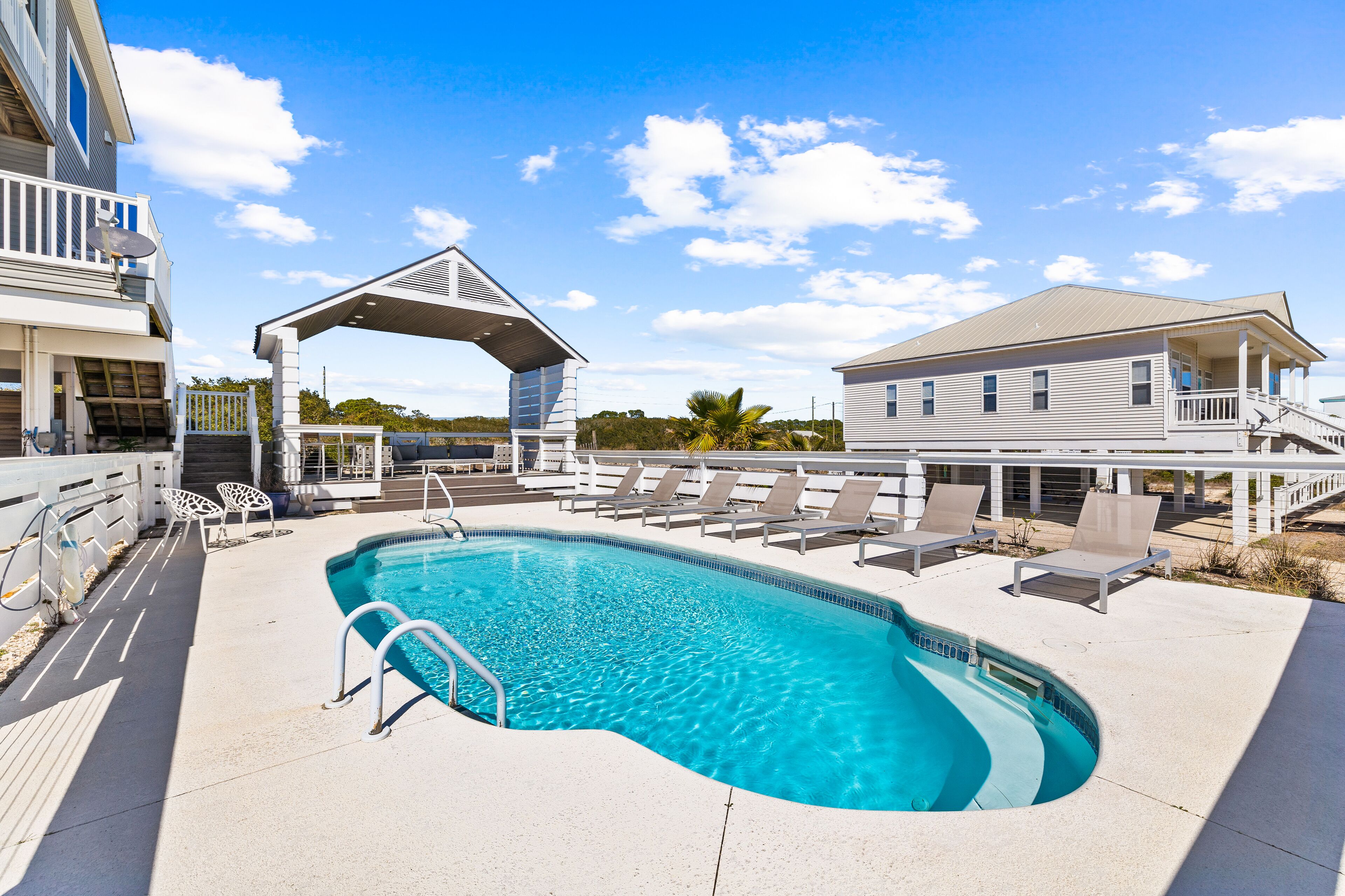 A swimming pool with lounge chairs and a covered area, surrounded by buildings.