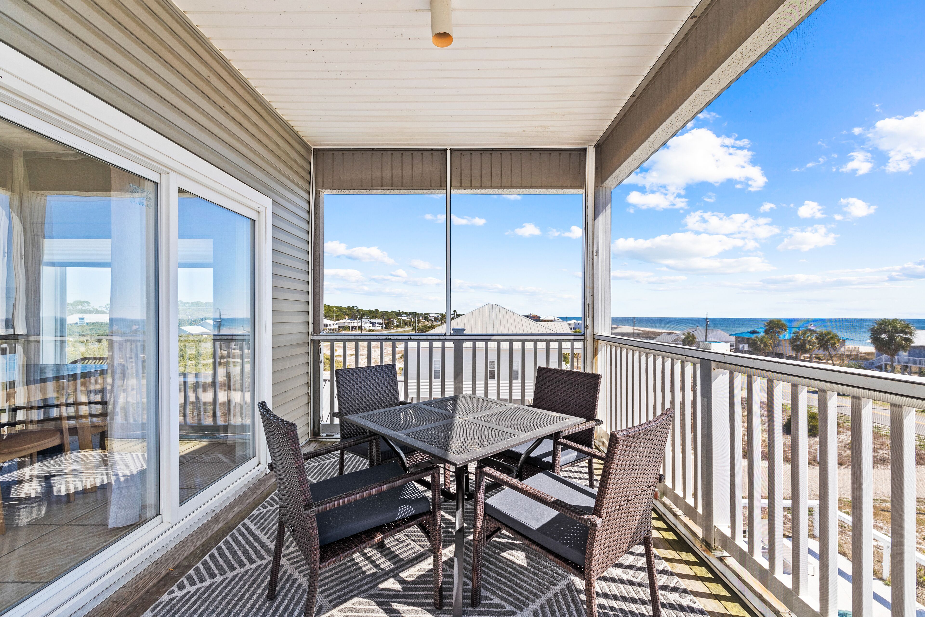 A covered outdoor balcony with a table and chairs, overlooking a beach and ocean.