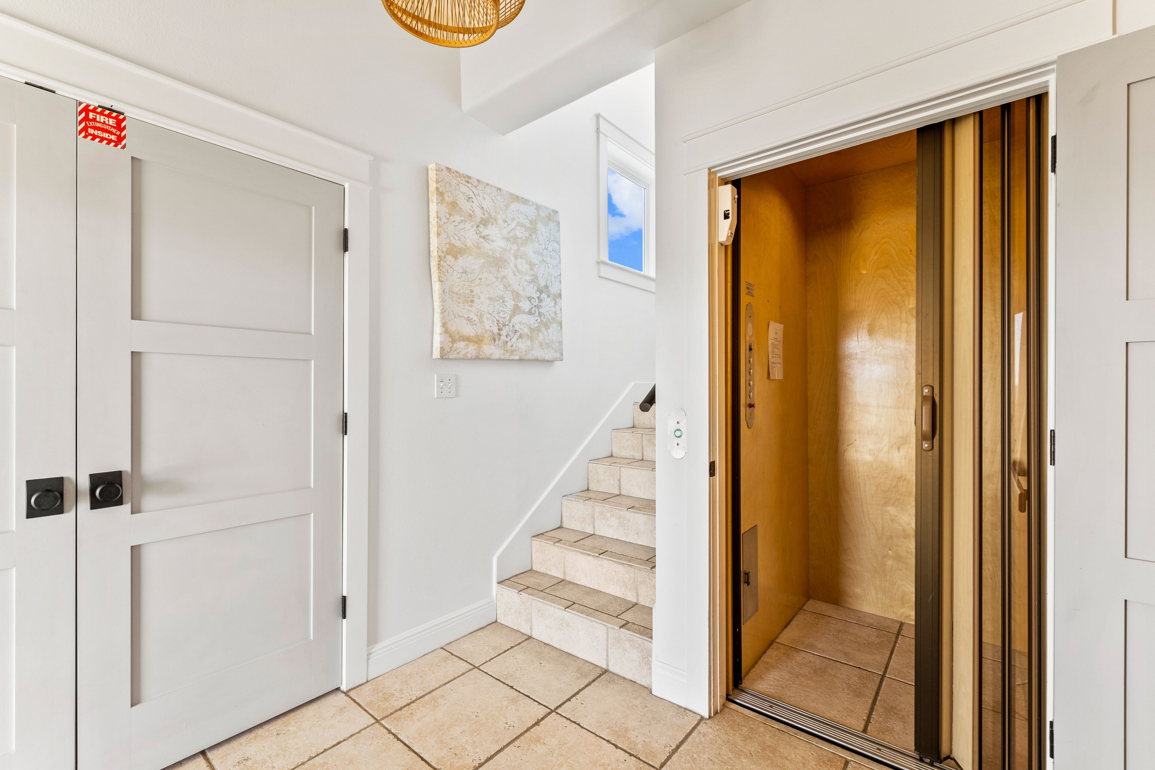 A hallway with a white door marked "FIRE EXIT," a staircase, and a wooden elevator.