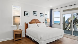 A bedroom with a large bed, wooden headboard, and a view of the ocean through a sliding glass door. - Above the Dune: 3 Bedroom, Beachfront, Sleeps 8 (St. George Island)