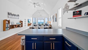 A modern kitchen with a central island, wooden shelves, and a view to the outside. - Above the Dune: 3 Bedroom, Beachfront, Sleeps 8 (St. George Island)