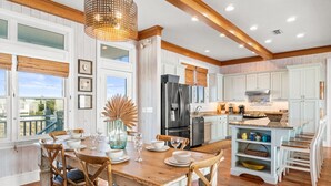 Una cocina amplia con pisos de madera, armarios blancos y un comedor con mesa y sillas de madera.