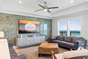 A living room with a large window, a ceiling fan, a sofa, a coffee table, and a decorative wall piece.