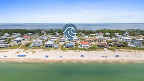 Eine Luftaufnahme einer Küstenwohngegend mit direkt am Strand gelegenen Häusern, darunter Häuser mit Meerblick sowie ein Sandstrand mit Sonnenschirmen.