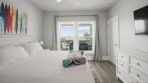 A bedroom with a bed, a ceiling fan, a window with curtains, a dresser, and a painting on the wall. - Blue Skies: Gulf Views, Private Pool, Pet Friendly (St. George Island)