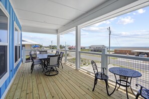 A covered outdoor area with a wooden deck, a table with chairs, and a view of the street and buildings in the background. - Blue Skies: Gulf Views, Private Pool, Pet Friendly (St. George Island)
