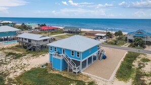 A coastal property with a prominent blue building featuring a balcony and a staircase, adjacent to a beach with a clear view of the ocean. - Blue Skies: Gulf Views, Private Pool, Pet Friendly (St. George Island)