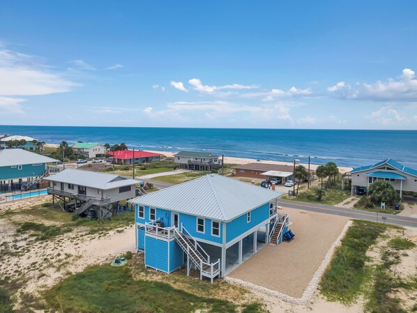 A coastal property with a prominent blue building featuring a balcony and a staircase, adjacent to a beach with a clear view of the ocean. - Blue Skies: Gulf Views, Private Pool, Pet Friendly (St. George Island)