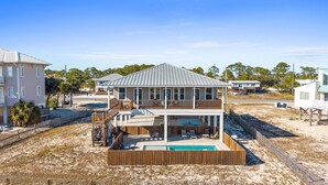 Een twee verdiepingen tellend huis aan het strand met een zwembad, een houten terras en een omheinde achtertuin.