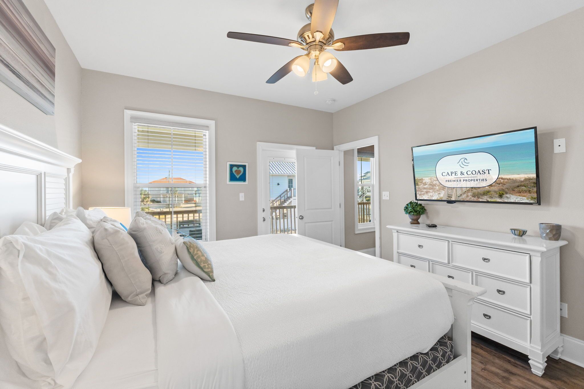 Un dormitorio con cama, ventilador de techo, televisor y vista a la playa.