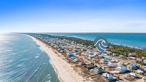 Luchtbeeld van een kustgebied met woningen langs het strand en een helder uitzicht op de oceaan.