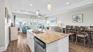 A modern kitchen with granite countertops, a dishwasher, and a dining area with wooden chairs and a table. - On the Half Shell: Beach View, Private Pool, One level Home (St. George Island)