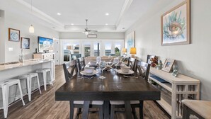 A spacious dining area with a dark wooden table set for four, surrounded by white barstools. - On the Half Shell: Beach View, Private Pool, One level Home (St. George Island)