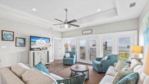 A spacious living room with a ceiling fan, a television, and a view of the outdoors through large sliding doors. - On the Half Shell: Beach View, Private Pool, One level Home (St. George Island)
