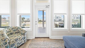 Une pièce avec un fauteuil à motifs, un canapé bleu et une vue sur l’extérieur, visible à travers une porte.