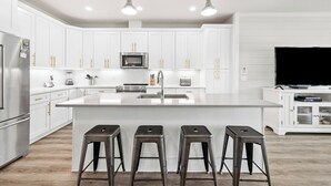Une cuisine moderne avec des meubles blancs, des appareils en acier inoxydable et un îlot central doté de tabourets de bar.