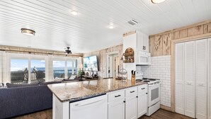 A modern kitchen with white cabinetry, a granite countertop, and a view of the ocean. - Sugar Magnolia: Beachfront SGI Home- Sleeps 12, Priv. Pool, Pet Friendly! (St. George Island)