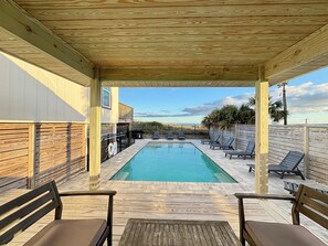 A covered outdoor swimming pool with lounge chairs and a wooden deck. - Sugar Magnolia: Beachfront SGI Home- Sleeps 12, Priv. Pool, Pet Friendly! (St. George Island)