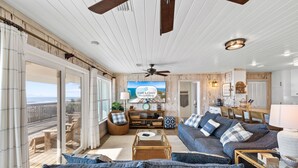 A spacious living room with a large television, comfortable seating, and a view of the ocean through large sliding glass doors. - Sugar Magnolia: Beachfront SGI Home- Sleeps 12, Priv. Pool, Pet Friendly! (St. George Island)