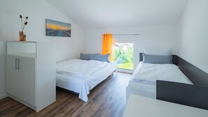 Un dormitorio moderno con dos camas individuales, un armario blanco y un ventanal con cortina naranja.